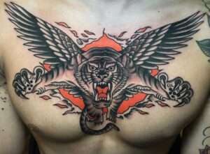An American traditional tiger with wings chest piece, exploding from an orange background with skin tears, by artist Travis Costello.