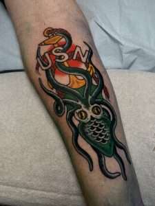 An American traditional classic anchor tattoo with USN being overtaken by a kraken / octopus below it tattooed by Jacksonville artist Julissa Yaselin, done in bright colors with bold lines.